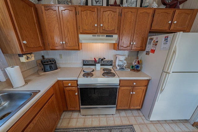 kitchen featuring under cabinet range hood, white appliances, light countertops, and brown cabinetry