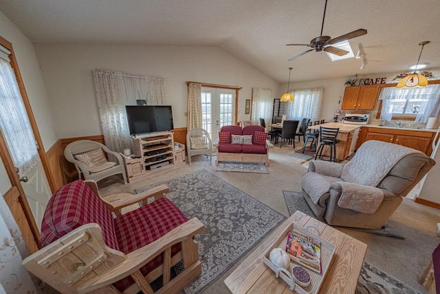 living room featuring a wealth of natural light, french doors, a wainscoted wall, and vaulted ceiling