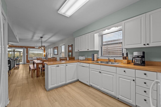 kitchen featuring white dishwasher, a peninsula, butcher block counters, a sink, and white cabinetry