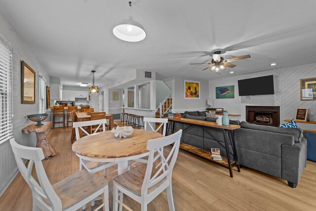 dining room with light wood finished floors, stairs, a ceiling fan, and a tiled fireplace