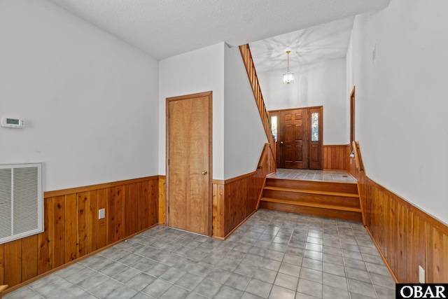 stairway featuring a notable chandelier, visible vents, wainscoting, wood walls, and a textured ceiling