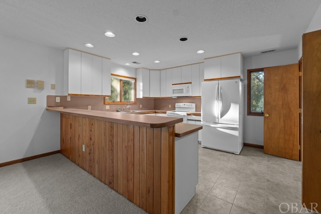 kitchen featuring white cabinets, a sink, white appliances, a peninsula, and baseboards