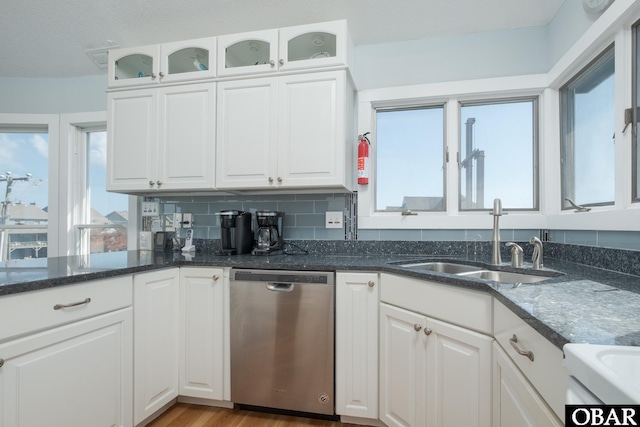 kitchen with stainless steel dishwasher, dark stone counters, white cabinetry, and a sink