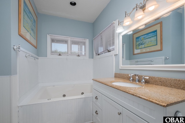 bathroom with a tub with jets, wainscoting, a textured ceiling, and vanity