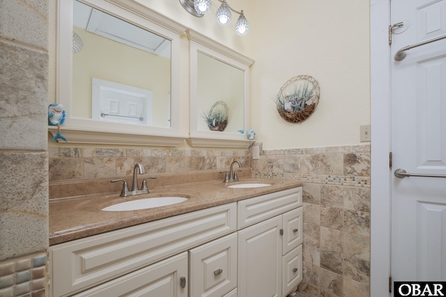 bathroom with double vanity, a wainscoted wall, tile walls, and a sink