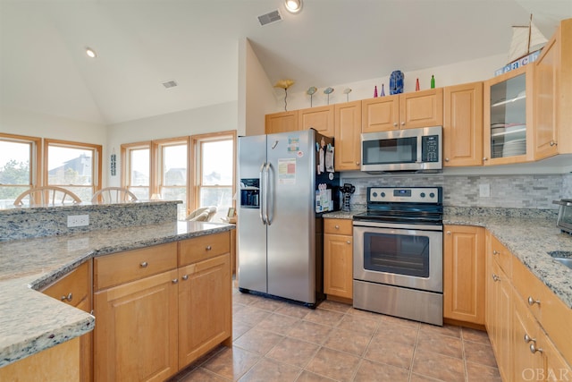 kitchen featuring vaulted ceiling, appliances with stainless steel finishes, backsplash, light stone countertops, and glass insert cabinets