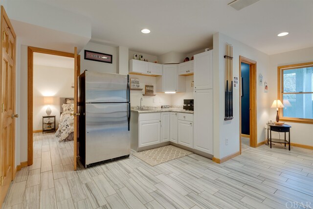 kitchen featuring wood finish floors, a sink, freestanding refrigerator, and white cabinets