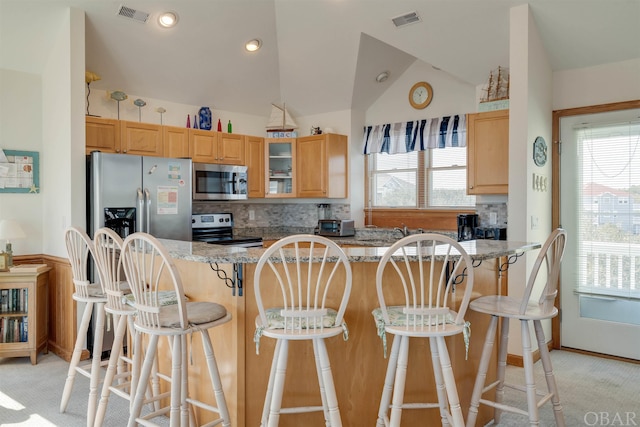 kitchen featuring light stone counters, a breakfast bar, visible vents, appliances with stainless steel finishes, and glass insert cabinets