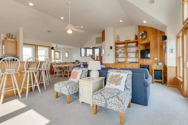 living room featuring lofted ceiling, wainscoting, a healthy amount of sunlight, and light carpet