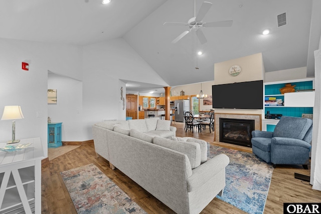 living room with high vaulted ceiling, ceiling fan with notable chandelier, visible vents, and wood finished floors