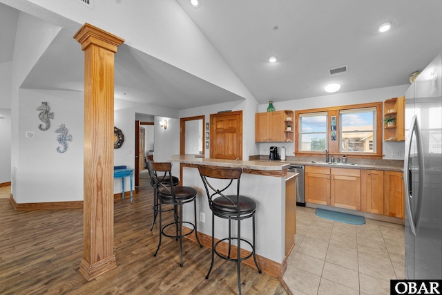 kitchen with stainless steel appliances, a breakfast bar, a sink, open shelves, and decorative columns