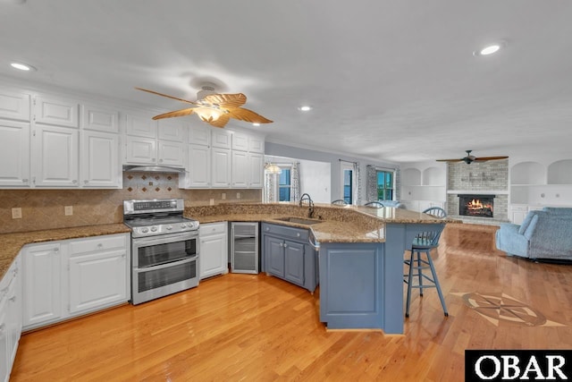 kitchen with a ceiling fan, a sink, white cabinetry, and range with two ovens