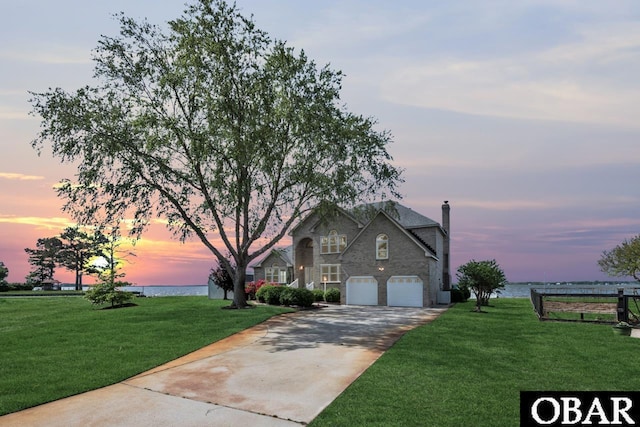 view of front facade featuring a water view, stone siding, a front yard, and concrete driveway