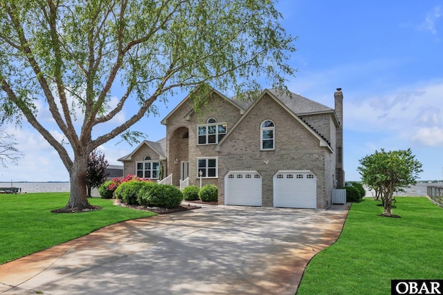 traditional-style house featuring a chimney, a front yard, brick siding, concrete driveway, and an attached garage