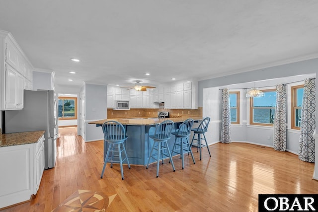 kitchen featuring appliances with stainless steel finishes, a breakfast bar area, white cabinetry, recessed lighting, and backsplash