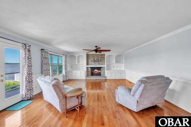 living area featuring a fireplace, a ceiling fan, built in shelves, and light wood-type flooring