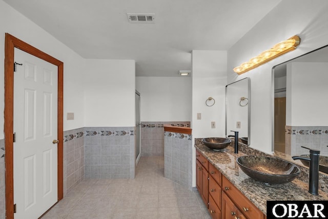 bathroom featuring visible vents, double vanity, tile patterned flooring, tile walls, and a sink