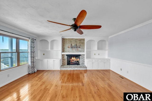 unfurnished living room with light wood-style floors, built in features, wainscoting, and a ceiling fan