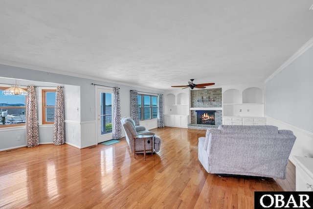 living room with a ceiling fan, built in features, a fireplace, light wood-type flooring, and ornamental molding