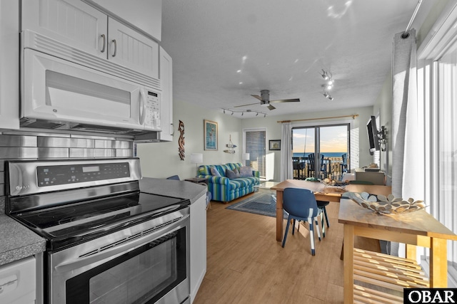 kitchen featuring stainless steel electric range oven, white microwave, light wood-style floors, open floor plan, and white cabinets