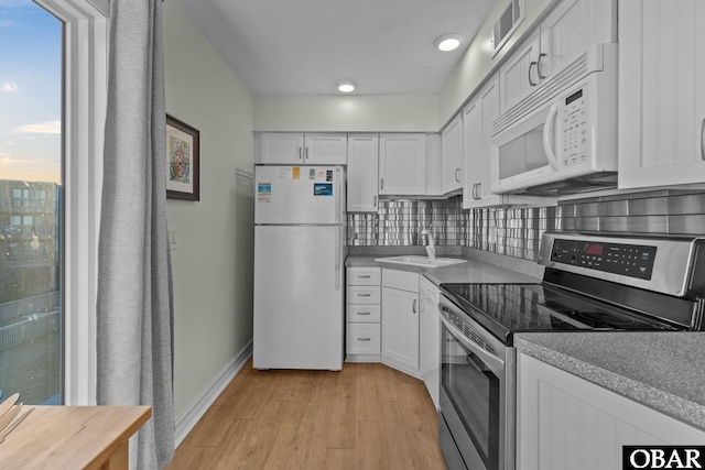 kitchen featuring white appliances, visible vents, white cabinets, and backsplash