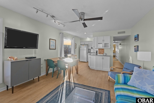 living room featuring light wood finished floors, visible vents, baseboards, and a ceiling fan