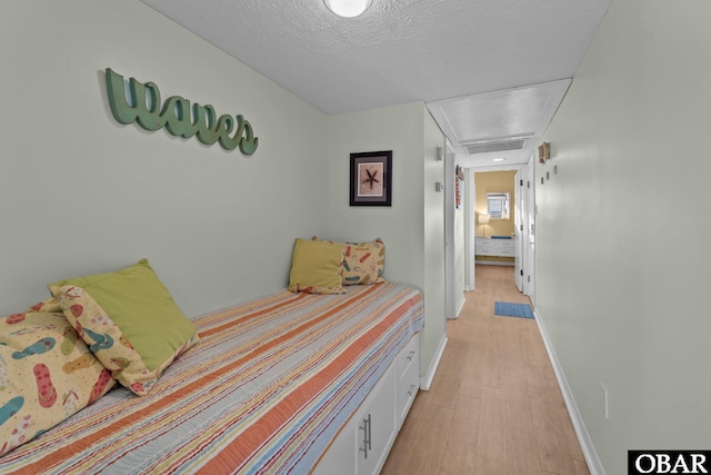 bedroom featuring baseboards, visible vents, a textured ceiling, and light wood finished floors