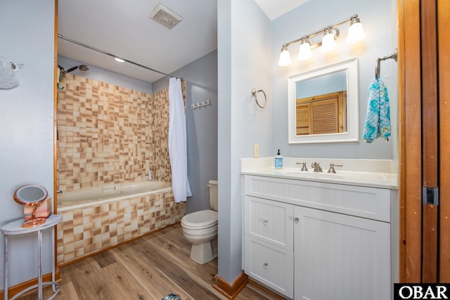 bathroom featuring tiled shower / bath, visible vents, toilet, vanity, and wood finished floors