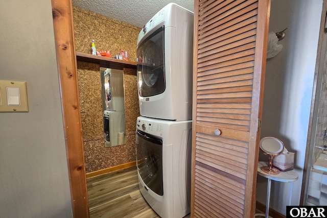 laundry area with a textured ceiling, stacked washer / dryer, wood finished floors, and baseboards