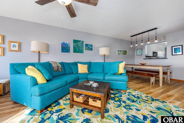 living area with ceiling fan, a textured ceiling, track lighting, wood finished floors, and baseboards