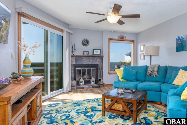 living room with a textured ceiling, ceiling fan, a tiled fireplace, and wood finished floors