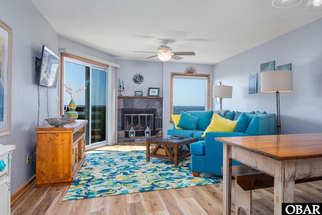 living area featuring ceiling fan, a fireplace, a textured ceiling, and wood finished floors