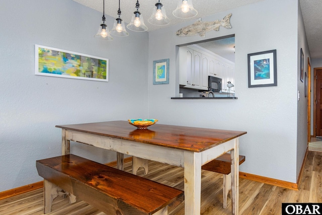 dining space with light wood-type flooring, a textured ceiling, and baseboards