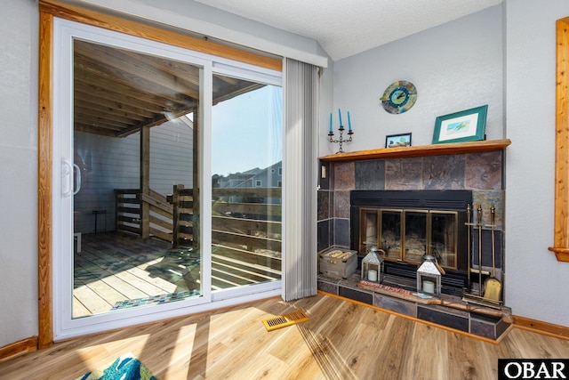 interior space featuring visible vents, baseboards, a tiled fireplace, wood finished floors, and a textured ceiling