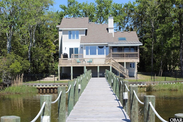 back of property featuring a deck with water view, fence, a sunroom, stairway, and a chimney