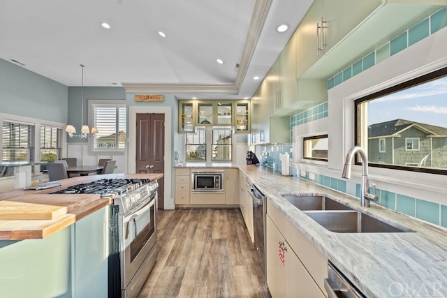 kitchen with stainless steel appliances, a sink, light stone countertops, light wood finished floors, and glass insert cabinets