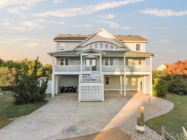 coastal home with a shingled roof, stairway, a carport, and concrete driveway