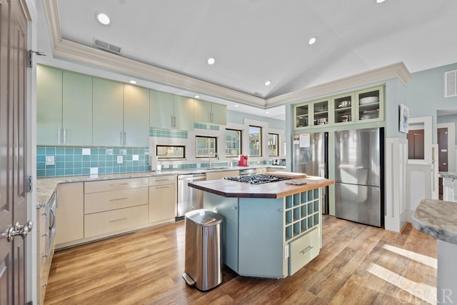 kitchen with a center island, a raised ceiling, appliances with stainless steel finishes, glass insert cabinets, and wood counters