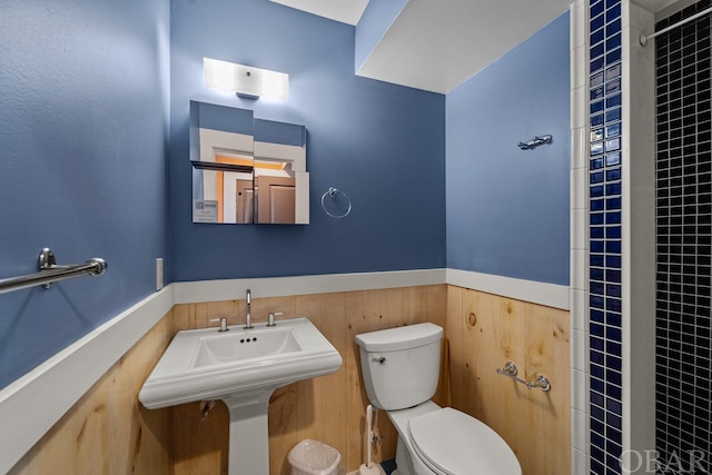 bathroom with toilet, wood walls, and wainscoting