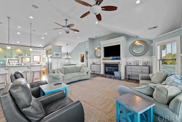 living area featuring a wainscoted wall, visible vents, vaulted ceiling, wood finished floors, and a tile fireplace