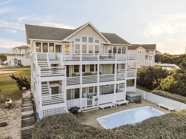 rear view of house with a patio, fence, roof with shingles, board and batten siding, and a hot tub