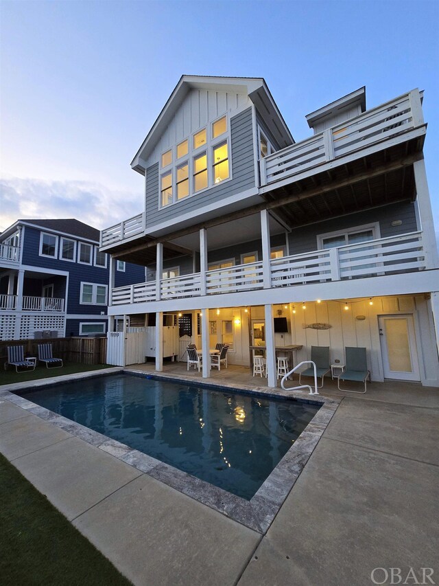 back of property with board and batten siding, a patio area, an outdoor pool, and exterior bar