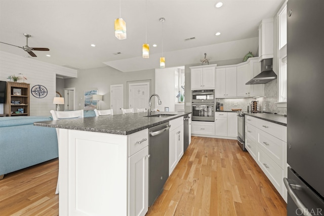 kitchen featuring stainless steel appliances, open floor plan, a kitchen island with sink, a sink, and white cabinets