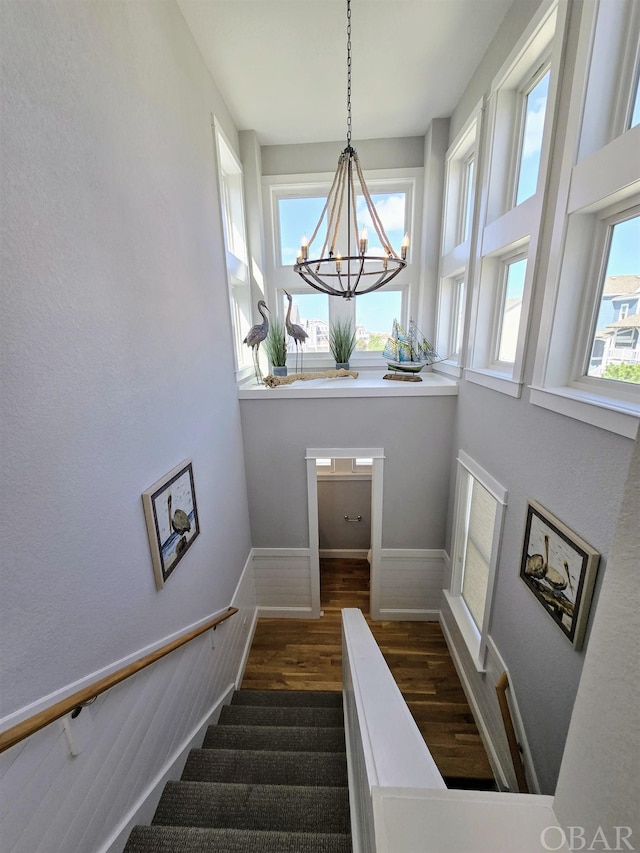 stairway featuring wood finished floors and an inviting chandelier