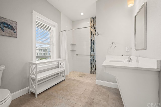 full bathroom with baseboards, toilet, tile patterned floors, a tile shower, and a sink