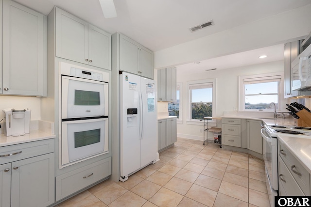 kitchen featuring visible vents, gray cabinets, a sink, white appliances, and light countertops