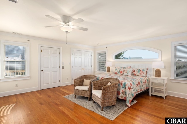 bedroom featuring visible vents, crown molding, baseboards, wood finished floors, and a ceiling fan