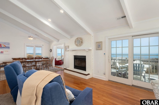 living room featuring a ceiling fan, wood finished floors, visible vents, lofted ceiling with beams, and a fireplace