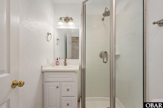 bathroom featuring vanity, a textured wall, and a stall shower