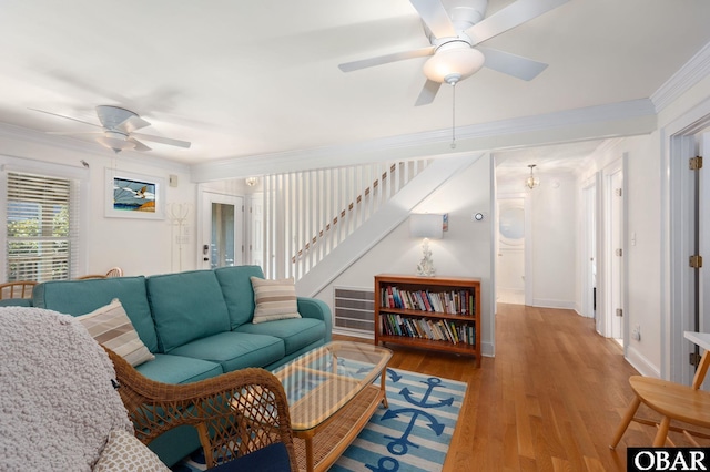 living area with ornamental molding, wood finished floors, baseboards, ceiling fan, and stairs